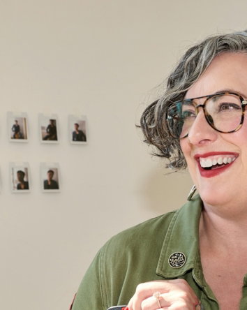 Smiling woman puts device into her patched olive green jacket.
